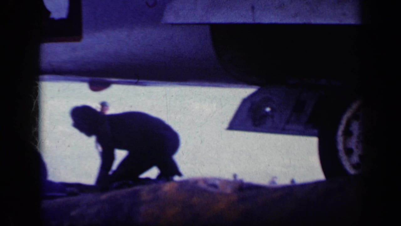 Deck crew member crouches beside an aircraft undercarriage on a sunlit carrier deck.