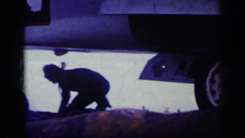 A crew member works low beside the underside and wheel area of an aircraft on a carrier deck, matching the supplied Cuba 1962 context.