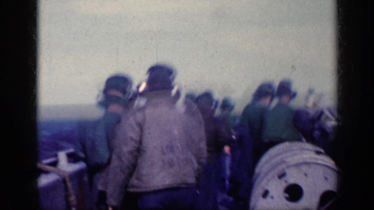 Sailors in headsets stand on a naval flight deck near equipment and a horizon line.