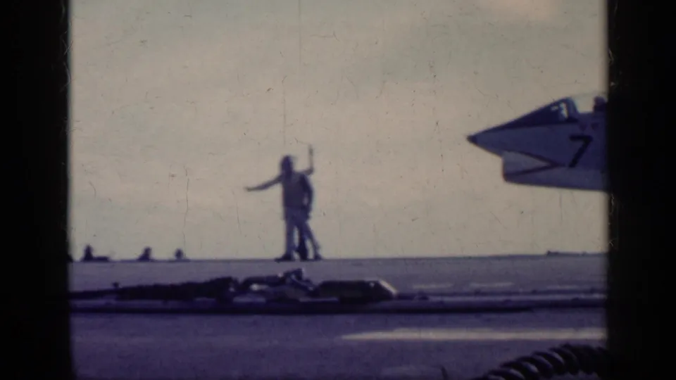 1962 Cuba-era 8mm frame showing deck crew signaling beside the nose of a U.S. Navy jet on a carrier deck.