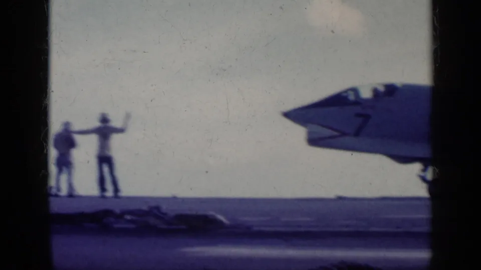 1962 8mm frame near Cuba showing deck crew hand signals beside the nose of a U.S. Navy jet on an aircraft carrier.