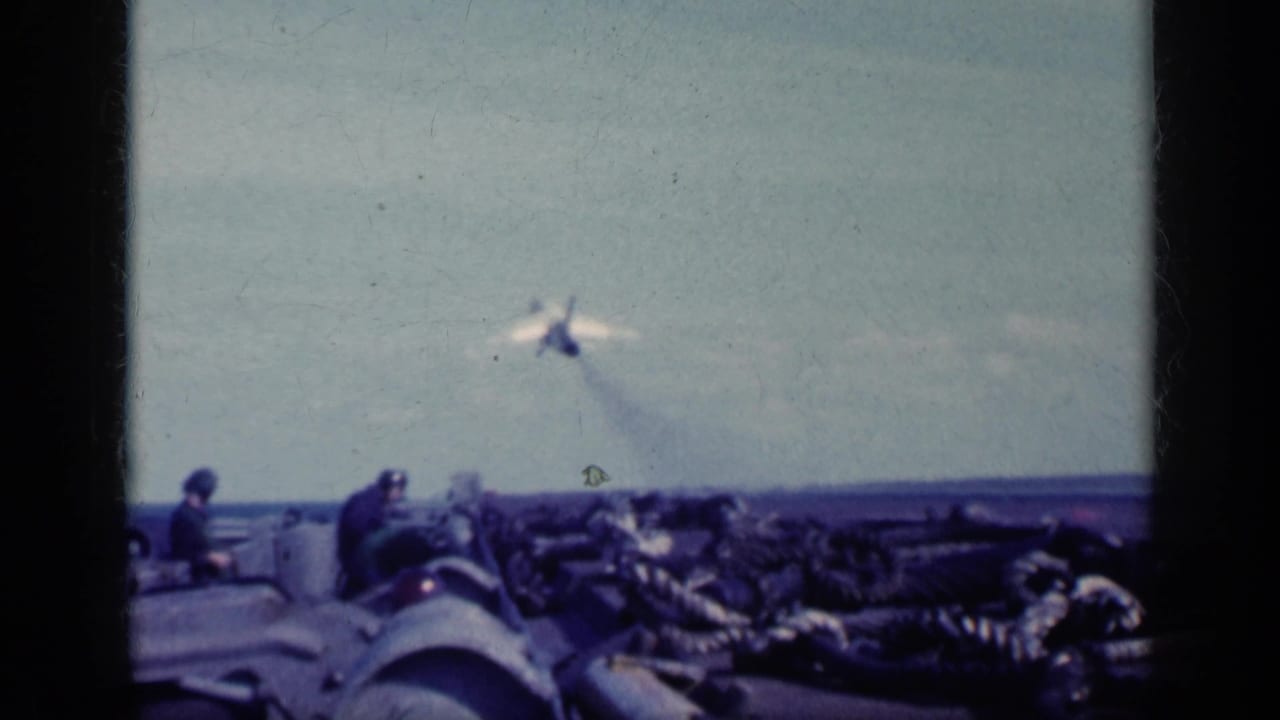 1962 Cuba-labeled 8mm frame showing a military jet just beyond the carrier deck, with deck crew and equipment in the foreground.