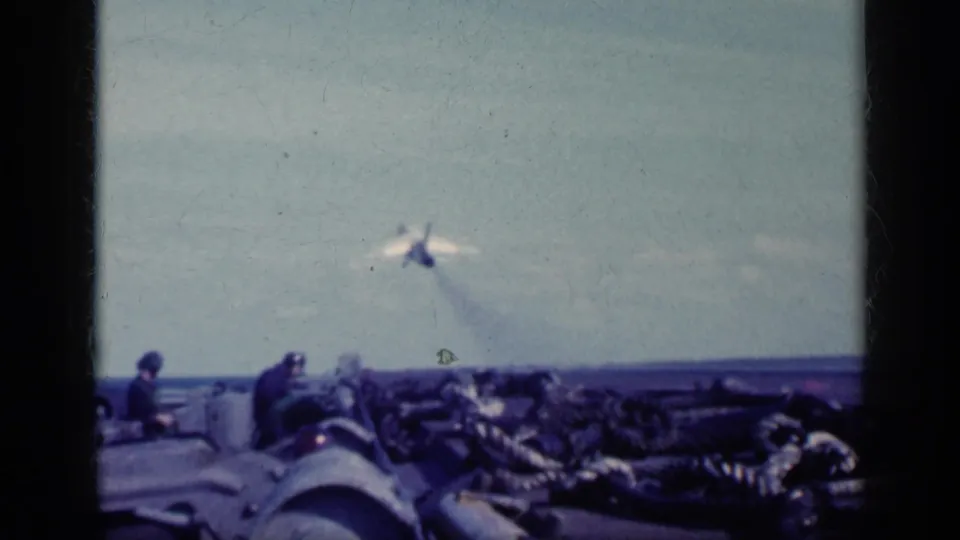 1962 Cuba-labeled 8mm frame showing a military jet just beyond the carrier deck, with deck crew and equipment in the foreground.