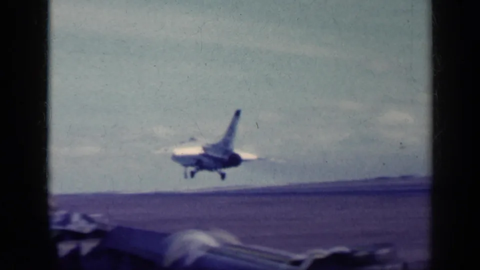 1962 Cuba-labeled 8mm frame showing a military jet airborne near the carrier deck, framed by dark film borders and a distant horizon.