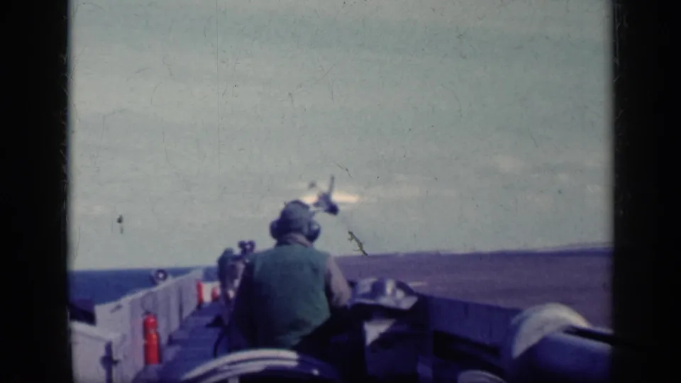1962 Cuba-labeled 8mm frame showing a helmeted crew member on the carrier deck as a jet appears beyond the deck edge.