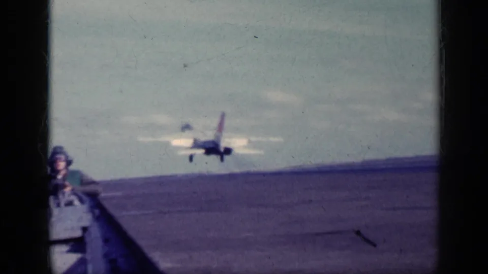 1962 Cuba metadata context: a military jet is seen beyond the aircraft carrier deck while a helmeted crew member stands near the camera.