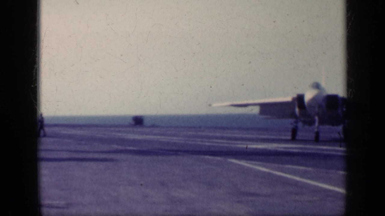 1962 Cuba-linked 8mm frame showing a jet on or near a carrier flight deck, with deck markings, ocean horizon, and film frame borders.