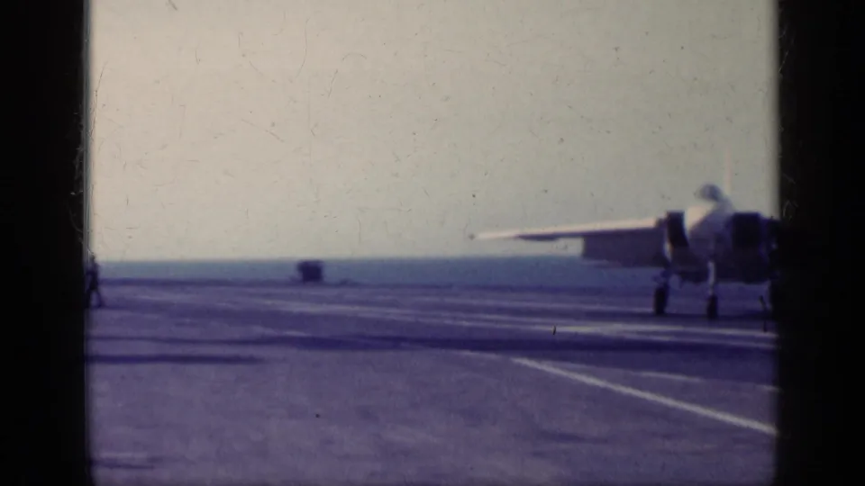 1962 Cuba-linked 8mm frame showing a jet on or near a carrier flight deck, with deck markings, ocean horizon, and film frame borders.