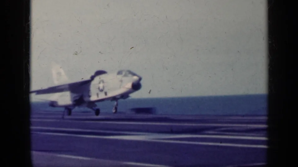 1962 Cuba-linked 8mm frame of a jet appearing to lift from an aircraft carrier deck, with the sea and sky behind it.