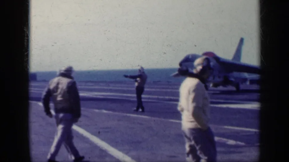 1962 Cuba-related 8mm frame showing carrier deck personnel near a naval jet, with one person signaling and another closer to the camera.