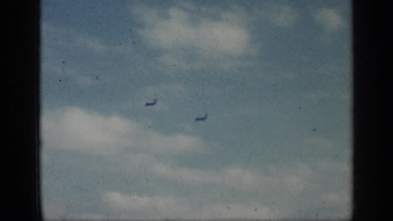 Two small jets fly in a cloudy sky with dark film-frame borders.