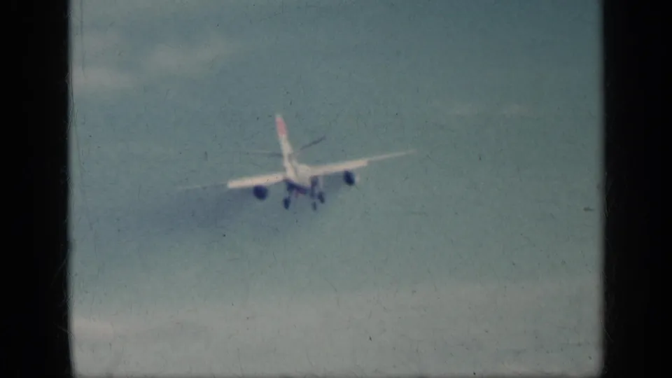 Distant commercial aircraft descends through a pale sky in 1962 Cuba footage, with landing gear visible.