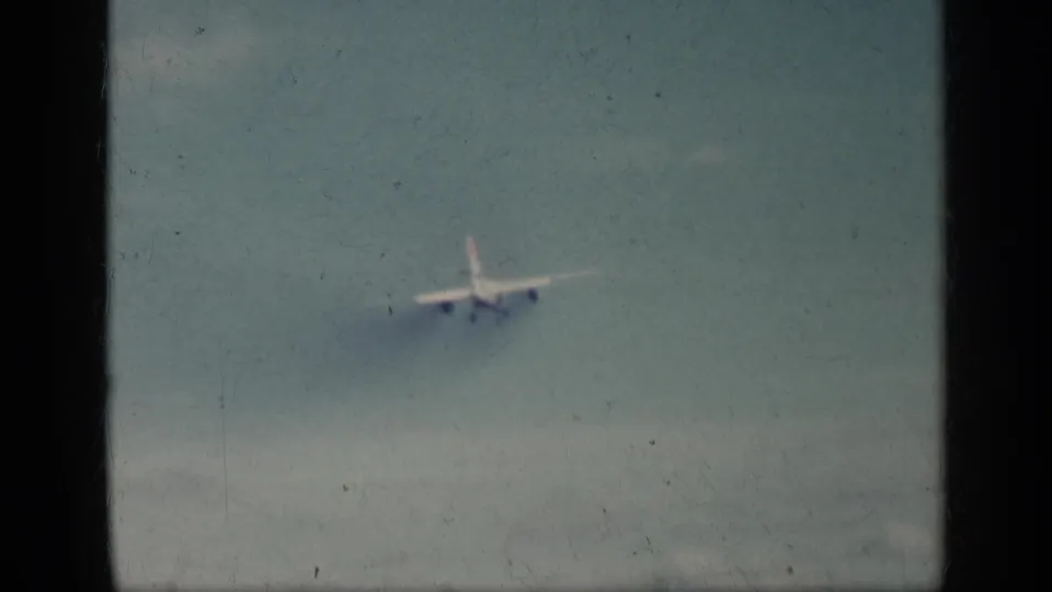 Home-movie view of a commercial aircraft descending toward a runway area in Cuba, softened by 8mm grain and fade.