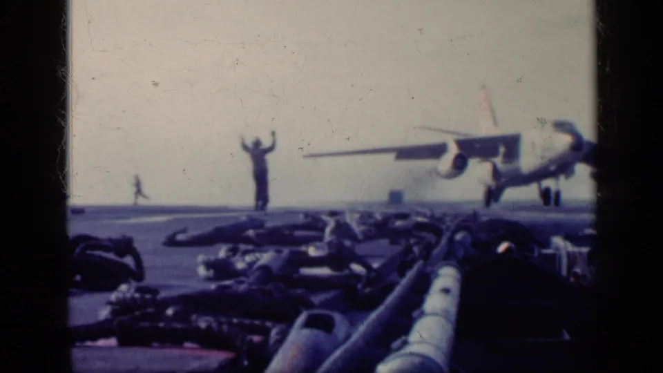 Faded 8mm frame from the supplied 1962 Cuba clip showing a carrier deck signaler and a jet close to the deck.