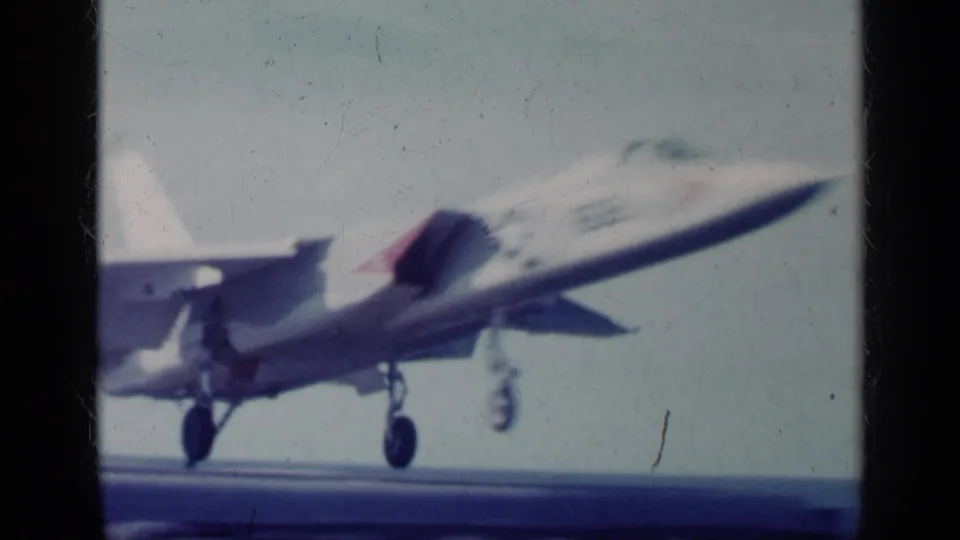 1962 Cuba-related 8mm frame showing a military jet just after takeoff from a carrier deck, landing gear extended against sky and sea.