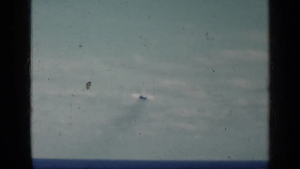 A distant military aircraft recedes over open water in a soft, color-faded 8mm frame tied to Cuba in 1962 metadata.