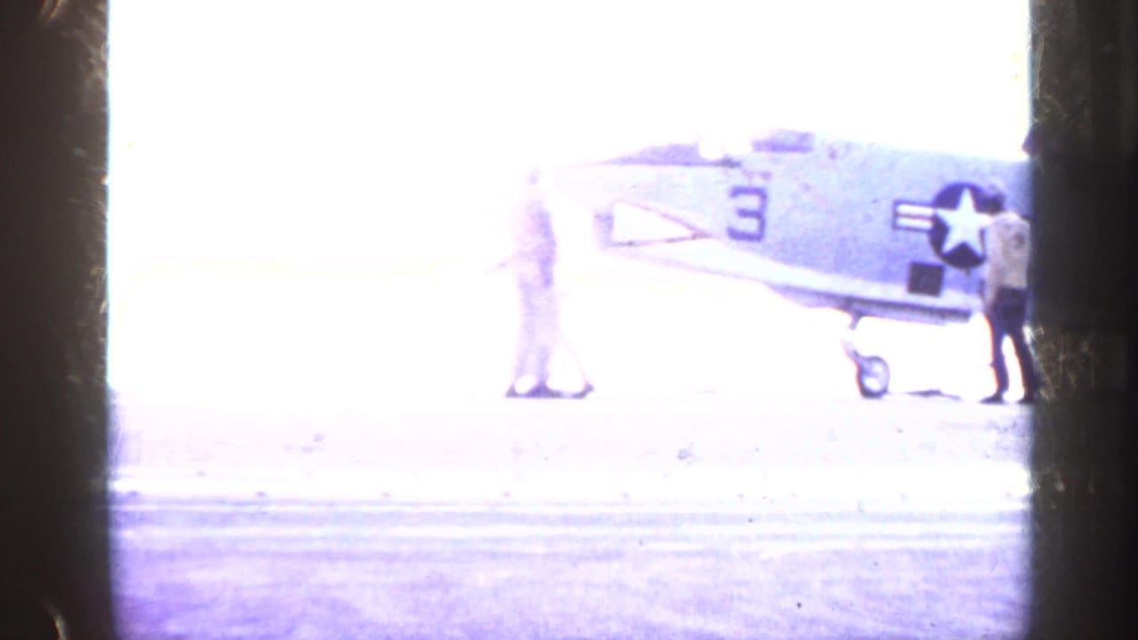 Overexposed aircraft carrier deck with a U.S. Navy jet and crew members near the fuselage.