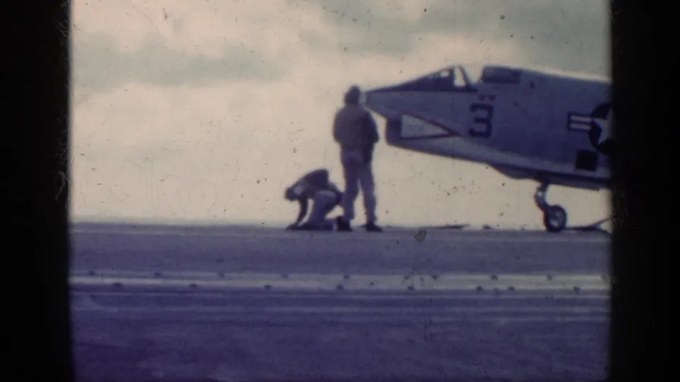 U.S. Navy jet on an aircraft carrier deck near Cuba in 1962 metadata, with one crew member crouched near the landing gear.