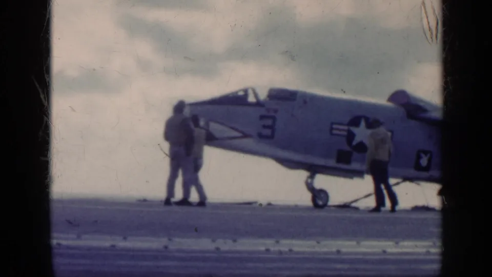 Side view of the U.S. Navy aircraft marked number 3, with deck crew positioned near the nose and mid-fuselage on the carrier deck.