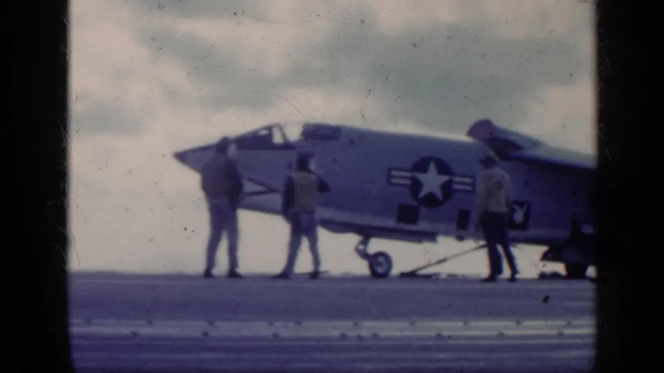 Carrier-deck view of the U.S. Navy jet and three crew members, with the star insignia and number 3 visible on the fuselage.