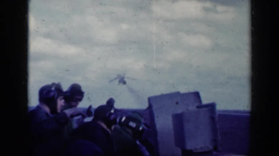 Helmeted observers watch as a military jet climbs beyond the deck in blue-tinted 1962 Cuba-associated 8mm footage.