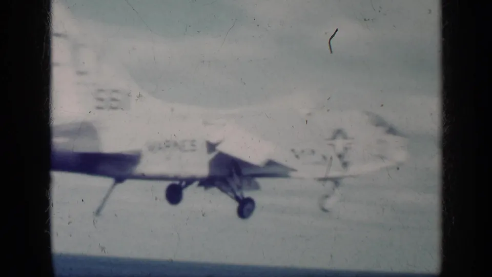 1962 Cuba-associated 8mm frame showing a light aircraft with partial military markings near a carrier deck and ocean horizon.