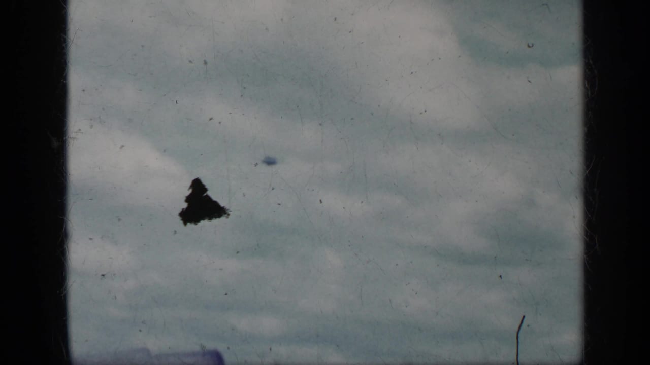 Cuba 1962 8mm frame showing cloudy sky over a shipboard view with a dark aircraft silhouette or film mark near the left side.