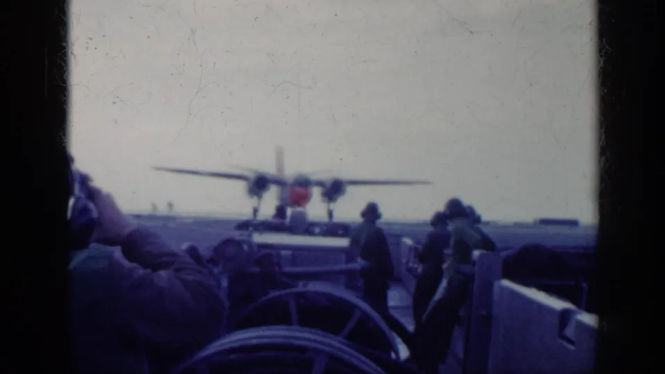 1962 Cuba 8mm frame of a red-nosed twin-engine aircraft on a ship deck, with crew members standing near deck equipment.