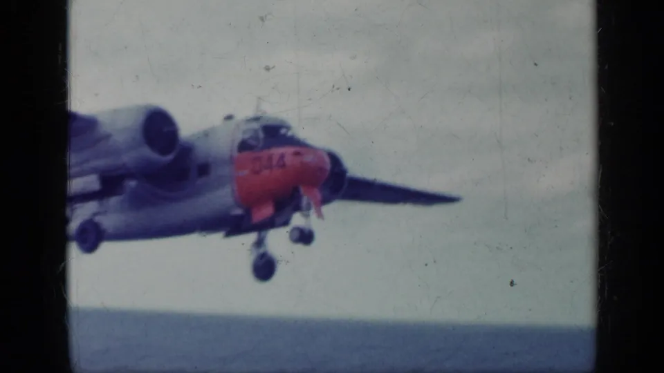 1962 Cuba 8mm frame of a red-nosed twin-engine aircraft airborne over the sea, with landing gear still down and an overcast horizon behind it.
