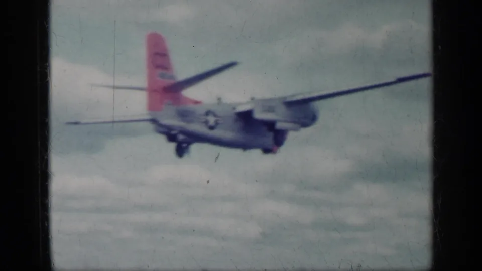 1962 Cuba archival frame of a marked twin-engine military aircraft flying over water, with red tail and U.S. star insignia visible.