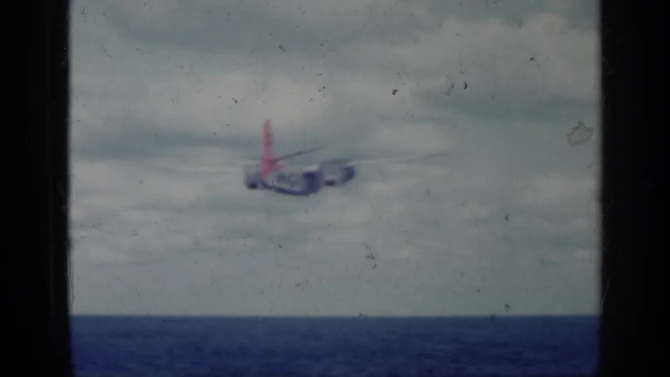 1962 Cuba archival frame showing the military aircraft receding over water, with red tail visible against a cloudy sky.