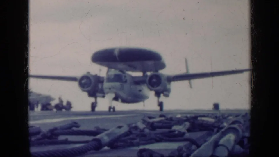 1962 Cuba-labeled 8mm frame showing a radar aircraft low over the carrier deck, with landing gear down and deck gear in the foreground.