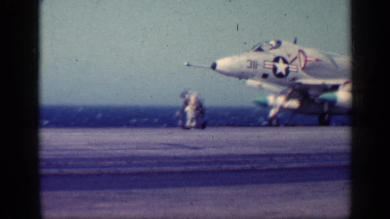 1962 Cuba metadata frame showing a U.S. Navy jet on a carrier deck, with crew figures nearby and the open ocean in the background.