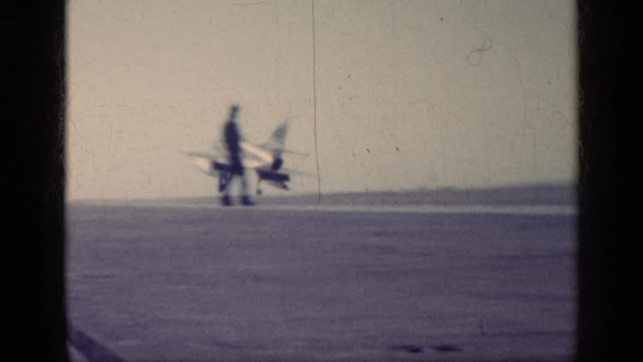 Distant 1962 carrier-deck view near Cuba showing a U.S. Navy jet and a person standing on the runway area.