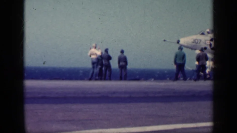 Crew members watch near a marked U.S. Navy jet on an aircraft carrier deck in the supplied 1962 Cuba footage.