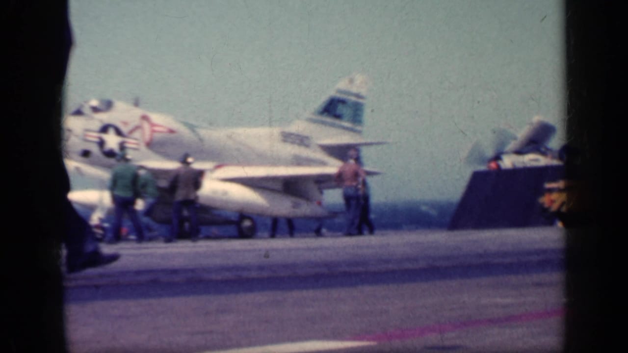 Early 1960s carrier-deck view showing a U.S. Navy jet, crew members, deck equipment, and sea horizon, supported by Cuba 1962 metadata.