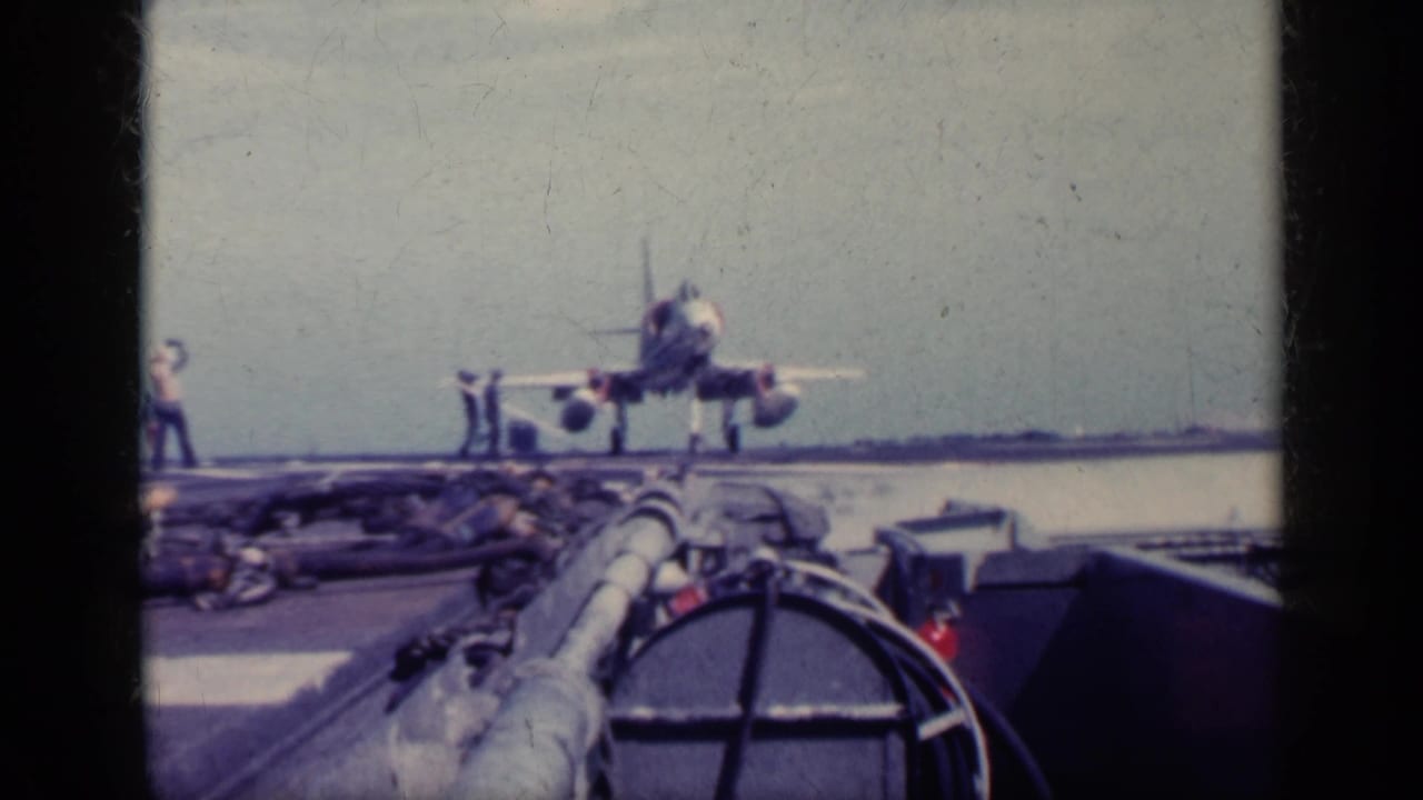 1962 Cuba metadata-supported 8mm frame showing a military jet on a carrier deck, viewed from a low angle with crew and sea visible.