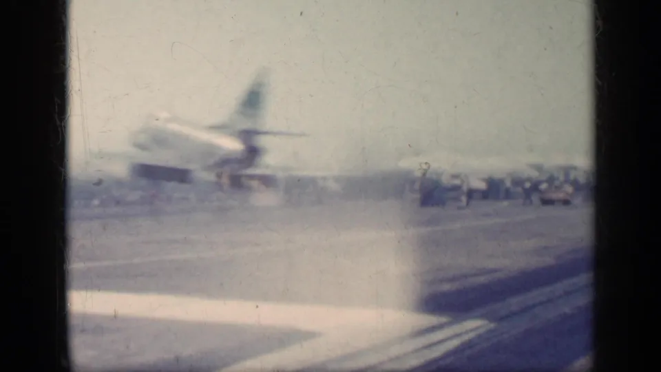 A U.S. Navy jet appears to accelerate on a carrier deck at sea, with haze near the runway and distant people visible.
