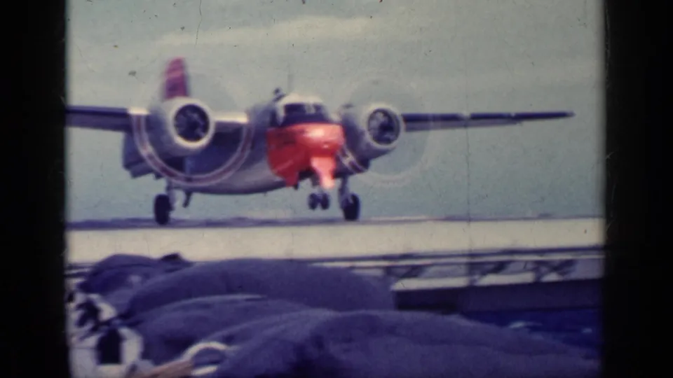 1962 Cuba-labeled 8mm frame of a twin-engine propeller aircraft moving closer on an aircraft carrier deck, with soft focus and color fading.