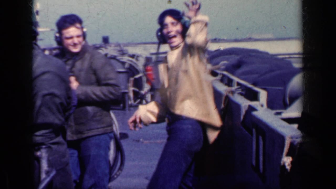 Adult men in heavy jackets stand on a ship flight deck near aircraft equipment.