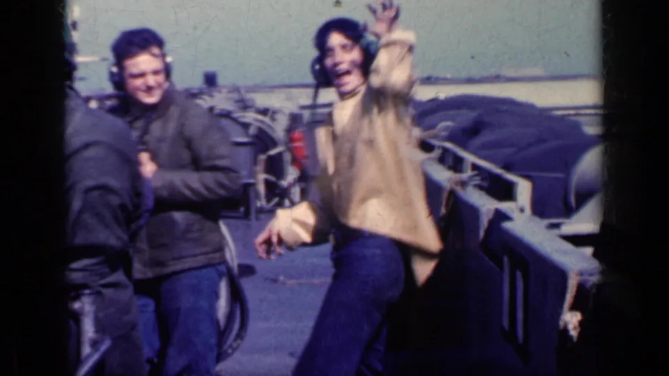 1962 Cuba metadata supports this view of adult military men on a ship flight deck, with one man waving near deck equipment.