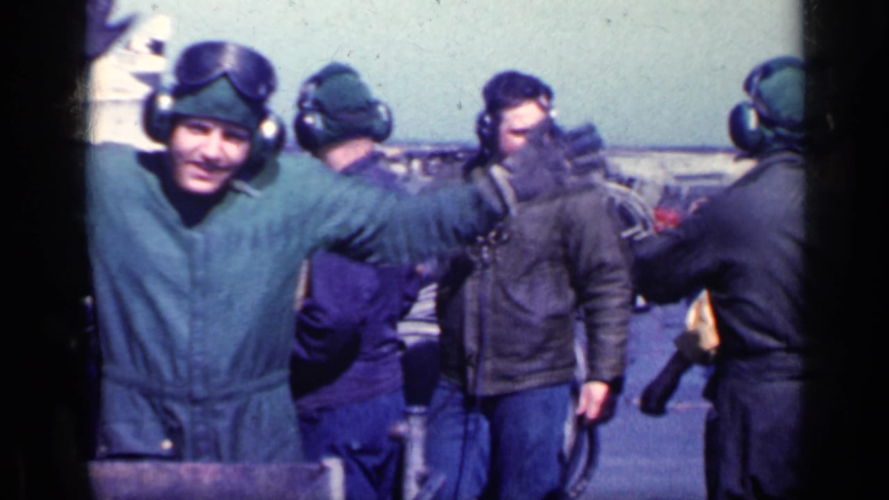 Flight crew in winter caps and goggles gather on an airfield deck.