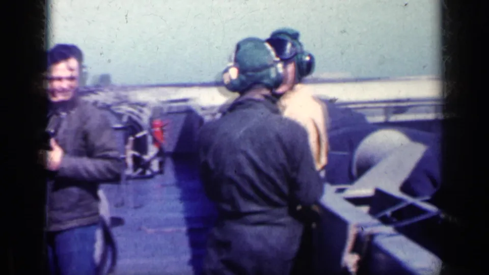 A man in a dark jacket smiles near other flight crew wearing caps and headsets on an airfield deck in Cuba 1962 footage.