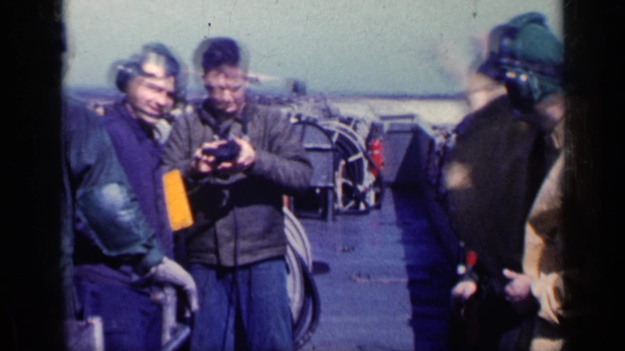 Men wearing ear protection stand on an aircraft carrier deck near equipment.