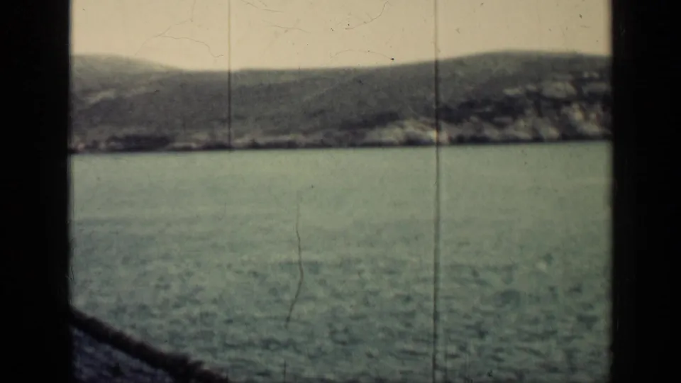 The clip ends on a grainy 8mm view of water and a low Cuban coastline, framed by dark film or camera-edge shadows.