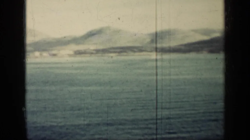 1962 Cuba coastal view across blue water toward pale mountains, partially divided by a dark onboard frame.