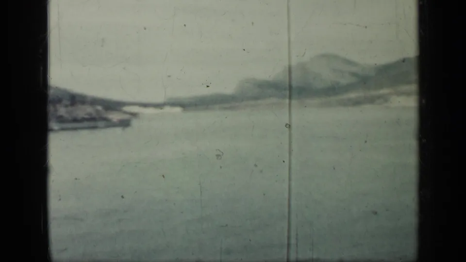 1962 Cuba 8mm frame with a distant shoreline across calm water, hazy hills, pale sky, and visible vertical film marks.