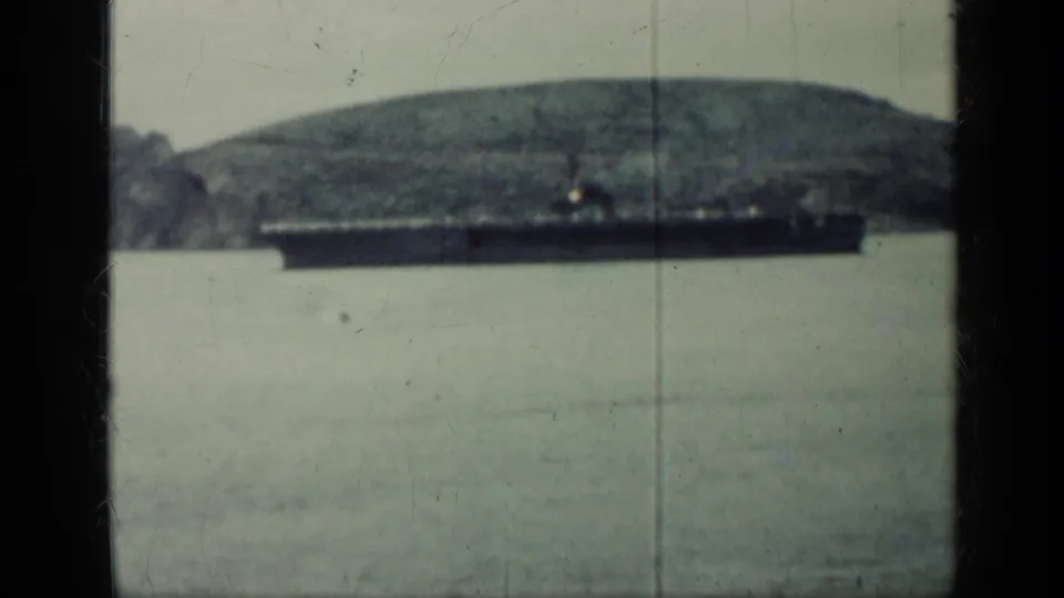 1962 Cuba 8mm frame of a large ship near a distant shoreline, backed by hazy hills and muted green-gray water.
