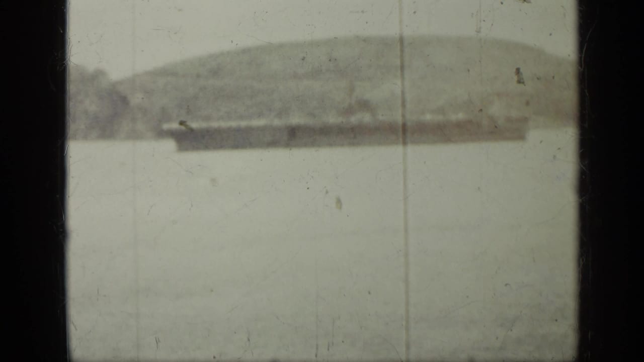 Soft 8mm frame from the supplied Cuba 1962 clip, with a distant shoreline or ship form partially visible through heavy exposure and film wear.