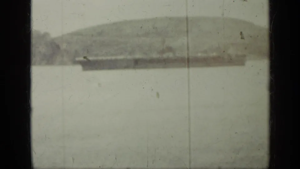 Soft 8mm frame from the supplied Cuba 1962 clip, with a distant shoreline or ship form partially visible through heavy exposure and film wear.